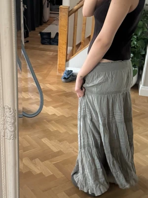 Grön långkjol med volangdetaljer - Säljer en snygg grön långkjol med volangdetaljer och resår i midjan. Kjolen har en avslappnad passform och är perfekt för dig som gillar en bohemisk stil. Materialet känns lätt och flowy, vilket gör den skön att bära under varmare dagar. Köpt på Nelly men finns inte längre kvar i frägen grön