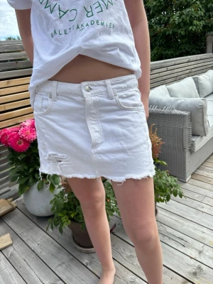 Vit lågmidjad jeanskjol - Säljer denna vita lågmidjadd jeanskjol med slitningar ifrån Zara! Kjolen är i storlek Xs men passar även S