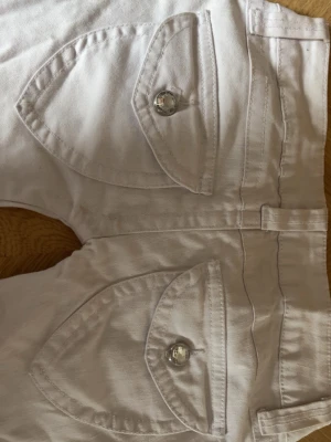 Lågmidjade vita jeans från Laura Scott - Säljer ett par vita jeans från Laura Scott med snygga ficklock och silverfärgade knappar både fram och bak. Jeansen har normal midja, bälteshällor och klassisk femficksdesign. Materialet är denim i bomull med lite stretch för skön passform.