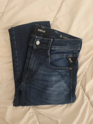 Mörkblå  jeans från Replay - Snygga mörkblå slim jeans från Replay med klassisk femficksdesign och diskreta slitningar framtill. Jeansen har en smal passform och är tillverkade i stretchigt denimtyg för extra komfort. Perfekta för en trendig och avslappnad look. W28 L32 knappt använda