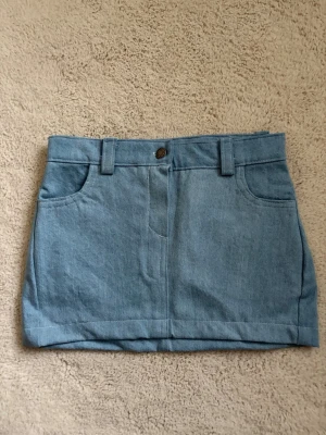 Blå jeanskjol med fickor - Har sytt den själv! Säljer en klassisk blå jeanskjol i kort modell med fram- och bakfickor samt hällor för bälte. Kjolen har knapp och dragkedja framtill och är gjord i ett mjukt denimtyg. Perfekt till sommaren och enkel att matcha med olika toppar.