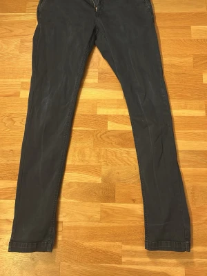 Mörkgrå slim fit chinos Replay - Snygga mörkgrå chinos från Replay, modell Zeumar med slim fit passform. Byxorna har klassisk design med dragkedjegylf och bälteshällor. Tillverkade i ett mjukt och stretchigt material för extra komfort.