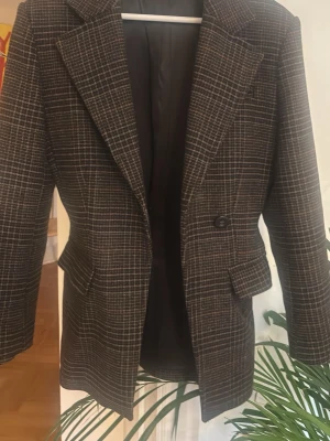 Rutig kavaj från & Other Stories - Snygg rutig kavaj från & Other Stories Paris Atelier i brunt och grått. Klassisk modell med breda slag, enkelknäppning och fickor med lock. Perfekt för att lyfta vilken outfit som helst med en tidlös och trendig look.
