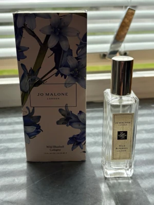 Jo Malone Wild Bluebell Cologne - En elegant parfym från Jo Malone, Wild Bluebell Cologne, i en genomskinlig glasflaska med silverfärgat lock. Doften är fräsch och blommig, perfekt för dig som gillar lätta och naturliga toner. Flaskan har en stilren, rektangulär form och exklusiv etikett. Endast testad 