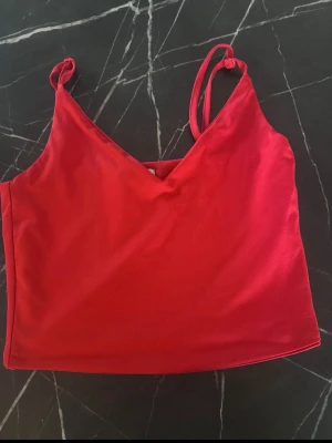 Röd croppad linnetopp med smala band - Snygg röd croppad linnetopp med smala axelband och v-ringad hals. Perfekt för varma dagar eller att styla lager på lager. Tillverkad i mjukt material som känns skönt mot huden.