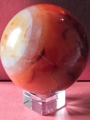 Karneol klot med glas ställ - Säljer en snygg dekorationskula i karneol med mixade färger i orange, vitt och rött. Kulan är polerad och har ett coolt mönster. Den kommer med en fyrkantig ställning i genomskinlig akryl som gör att kulan står stabilt och syns bra i rummet. 300 g, höjd 6 cm