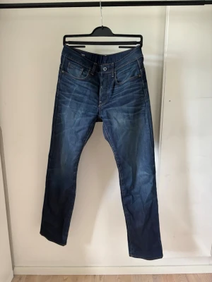 G star 3301 Straight - Snygga blå jeans i slim fit-modell med lätt slitna detaljer och klassisk femficksdesign. Jeansen har normal midja, dragkedjegylf och kontrastsömmar. Tillverkade i denim med en skön känsla och passform.