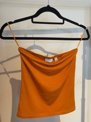 Orange axelbandslös topp - En orange tubtopp från Vero Moda, storlek XS. Fint skick, endast använd några gånger.