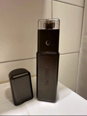 Tanrevel  spraytan - Säljer en  spraytan-enhet från Tanrevel i mörkbrun färg med stilren, fyrkantig design och genomskinligt lock. Perfekt för att enkelt få en jämn solbränna hemma eller på språng. Laddas via USB och är smidig att ta med sig.