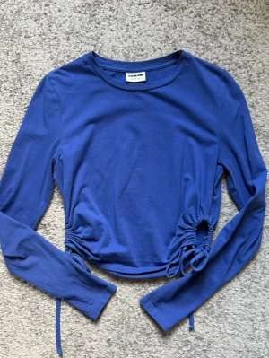 Blå croppad topp med snörning - Trendig blå croppad topp med långa ärmar och snygg snörningsdetalj i sidorna. Tillverkad i mjuk bomull som känns skön mot huden. Perfekt för dig som vill ha en enkel men ändå unik topp i garderoben.