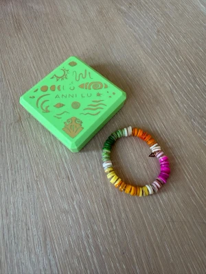 Färgglatt pärlarmband från Anni Lu - Säljer ett färgglatt armband från Anni Lu med platta pärlor i regnbågens färger som gult, grönt, orange, rosa och vitt. Armbandet har en elastisk tråd och en liten guldfärgad detalj. Perfekt för dig som gillar lekfulla accessoarer.