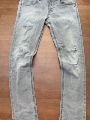 Dondup jeans  - Säljer ett par ljusgrå jeans med slitningar och lagade detaljer på framsidan. Jeansen har raka ben, klassisk femficksmodell och en tvättad look som ger en avslappnad vibe. Perfekta för dig som gillar en trendig och casual stil.