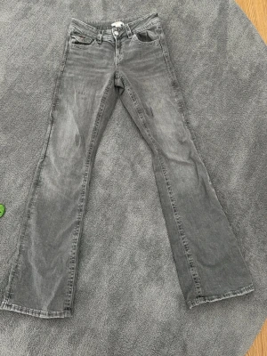 Grå bootcut jeans med slitningar - Snygga grå jeans med bootcut passform och klassisk femficksdesign. Jeansen har en lätt tvättad look med slitningar och normal midja. Perfekta för en avslappnad och trendig stil.