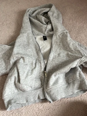 Grå zip hoodie med huva - Snygg grå hoodie från Stadium med dragkedja framtill och två fickor. Modellen har huva och ribbade muddar vid ärmslut och nederkant. Perfekt för en avslappnad och trendig look. Tillverkad i mjukt bomullsmaterial.