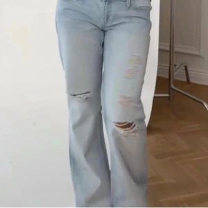 Ljusblåa raka jeans med slitningar - Säljer ett par ljusblå jeans med raka ben och trendiga slitningar på låren och knäna. Jeansen har låg midja och klassisk femficksdesign. Perfekta för en avslappnad och cool stil.