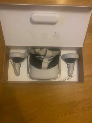 Oculus Quest 2 VR-headset med kontroller - Säljer ett Oculus Quest 2 VR-headset i vitt med tillhörande två handkontroller. Headsetet har justerbart band och modern design. Perfekt för gaming och VR-upplevelser. Materialet är plast och banden är i tyg. En kontroll har stick drift, men går lätt att lösa!