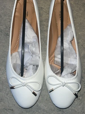 Vita ballerinaskor med rosett - Klassiska vita ballerinaskor med rund tå och dekorativ rosett framtill. Skorna har en slät ovandel och vadderad innersula för extra komfort. Splitternya, säljer då jag föredrog ett annat par. Kan självklart diskutera pris🤍