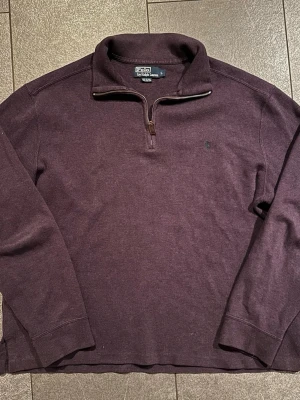 Mörklila halvzip från Polo Ralph Lauren - Snygg mörklila tröja från Polo Ralph Lauren med halv dragkedja och hög krage. Tillverkad i 100% bomull och har diskret logga broderad på bröstet. Perfekt för en avslappnad men stilren look.