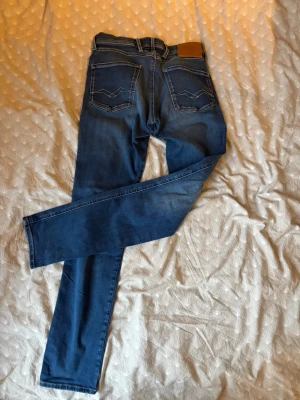 Replay Anbass Hyperflex jeans blå 28/32 - Säljer ett par Replay Anbass Hyperflex jeans i klassisk blå tvätt. Slim fit-modell med fem fickor, snygga kontrastsömmar och stretchigt material för extra komfort. Märkespatch bak i midjan. Perfekta jeans för dig som gillar stilren look. Jeansen är i mycket bra skick, näst intill nya.                                      Priset är ej hugget i sten.                        Packade och klara för försäljning.                  Bara att höra av dig vid minsta fundering Mvh