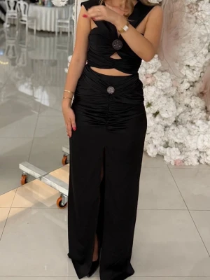 Cool BALKLÄNNING /bröllopsklänning - Svart långklänning med snygga cut-outs vid midjan och dekorativa knappar framtill. Klänningen har en djup v-ringning, slits framtill och är ärmlös. Materialet är glansigt och följsamt, perfekt för en trendig look.