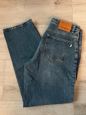 Blå raka jeans från Woodbird - Säljer ett par klassiska blå jeans från Woodbird med rak passform och fem fickor. Jeansen har en snygg vintage tvätt och är gjorda i slitstark denim. Perfekta för en avslappnad och trendig look.