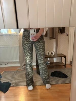 Leopardmönstrade utsvängda jeans - Säljer ett par snygga jeans med leopardmönster och utsvängda ben. Jeansen har hög midja och är i en gråbeige ton med mörkare fläckar. 