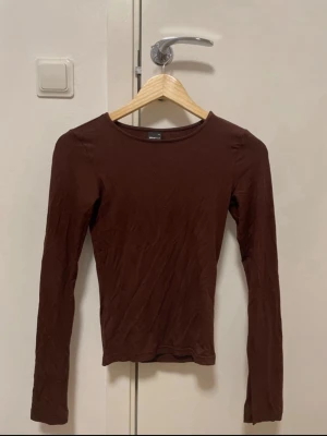 Brun topp med slits i ärmarna | XS från Gina Tricot - Säljer denna sjukt fina brun topp från Gina Tricot i storlek XS – sitter såå snyggt på kroppen och ger verkligen den där clean, effortless looken 😍  Perfekt basic men ändå inte basic yk, funkar till allt oavsett om du vill dressa upp eller köra casual ✨  Har dessutom snygga slitsar vid ärmarna som ger extra vibe och gör den lite mer unik 🤎