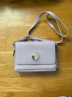 Ljusrosa axelväska från Don Donna - Snygg ljusrosa axelväska från Don Donna med justerbar rem och silverfärgad logodetalj på framsidan. Väskan är tillverkad i strukturerat syntetmaterial och har en praktisk dragkedja på sidan. Perfekt för dig som gillar stilrena accessoarer.