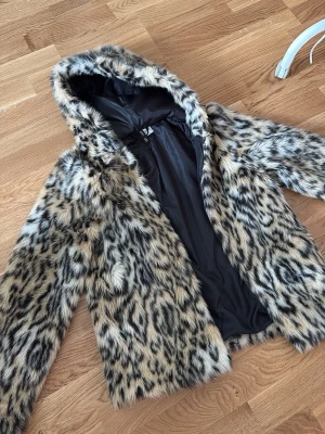 Leopardmönstrad pälsjacka med huva - Snygg leopardmönstrad pälsjacka från H&M med huva och svart innerfoder. Jackan har en fluffig känsla och stängs med dragkedja framtill. Perfekt för dig som vill sticka ut och hålla dig hyfsat varm. 