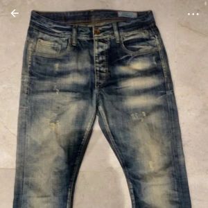 Jack N Jones Travis   31/34 - Snygga blå jeans från Jack & Jones med slitna detaljer och cool tvätt. Klassisk femficksmodell med kontrastsömmar och unika broderade bakfickor. Jeansen har normal passform och har storleken 31/34.