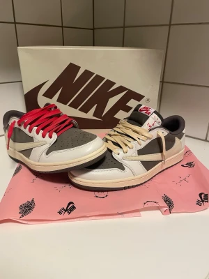 Nike x Travis Scott Reverse Mocha Air Jordan 1 Low  - Nike x Travis Scott Reverse Mocha Air Jordan 1 Low sneakers i brunt, vitt och beige läder med ikonisk omvänd swoosh. Ena skon har röda skosnören och den andra beige. Tungan har Nike Air-logga i rött och sulan är beige. Kommer med originalkartong och specialpapper. Samt extra snören. De är testade och knappast rörda. Kom dm för mer frågor. 