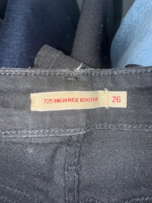 Levi's 725 High Rise Bootcut Jeans - Snygga svarta Levi's 725 High Rise Bootcut jeans i premiumkvalitet. Modellen har hög midja och bootcut-ben som ger en trendig siluett. Perfekta för dig som vill ha en klassisk men modern look. Tillverkade i ett mjukt och stretchigt material för extra komfort.