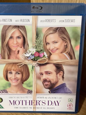 Mother's Day Blu-ray film - Mother's Day är en Blu-ray film i originalfodral med blå plast. Omslaget har bilder på flera kända skådespelare och en blomsterdekoration i mitten. Filmen är en varm komedi om relationer och familj, perfekt för dig som gillar romantiska och roliga filmer.
