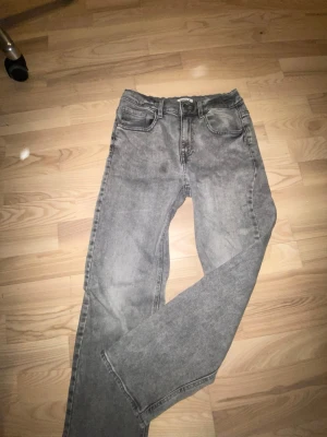 Grå raka jeans i vintage-stil - Säljer ett par grå jeans med rak passform och klassisk femficksdesign. Jeansen har en tvättad vintage-look. Perfekta för en avslappnad och trendig stil. 