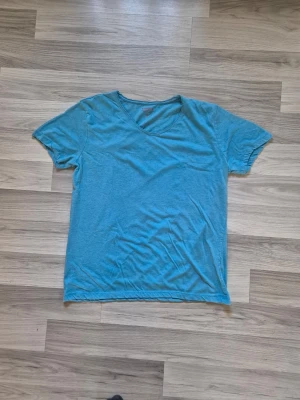 Blå basic t-shirt med v-ringning - Enkel blå t-shirt med v-ringad hals och korta ärmar. Perfekt för en avslappnad stil och lätt att matcha med andra plagg. Tillverkad i mjukt bomullsmaterial för skön komfort hela dagen.