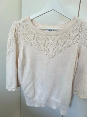 Vit stickad tröja med spetsdetaljer - Söt vit stickad tröja från Saint Tropez med fina spetsdetaljer upptill och på ärmarna. Tröjan har rund halsringning, trekvartsärmar och ribbade muddar. Perfekt för dig som gillar en romantisk och stilren look.