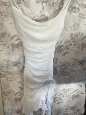 Vit omlottklänning med volang shein  - Säljer en vit, ärmlös klänning med omlottdesign och volangdetaljer nertill. Klänningen har smala axelband och en draperad, figurnära passform som ger en snygg siluett. Perfekt för sommarens alla tillfällen!