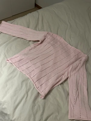 Ljusrosa stickad tröja med hålmönster - Söt ljusrosa stickad tröja med långa ärmar och dekorativa hålstickade ränder. Tröjan har en rak passform och är tillverkad i ett mjukt material som känns skönt mot huden. Perfekt för dig som gillar en feminin och avslappnad stil.