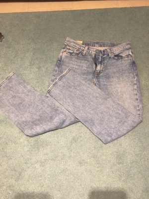 Ljusblå raka jeans från Levi's - Säljer ett par klassiska ljusblå jeans från Levi's med rak passform och hög midja. Jeansen har fem fickor, bälteshällor och dragkedja med knapp. Perfekta till vardags för en avslappnad och tidlös look.