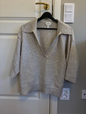 Beige stickad tröja med krage från HM - Stickad tröja i mjuk beige nyans från H&M. Tröjan har en bred krage och djup v-ringning, samt trekvartsärmar och ribbade muddar vid ärmslut och nederkant. Perfekt för lager på lager! 