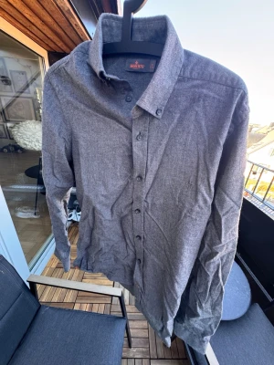 Najs grå skjorta från Morris🙌🤩 - Stilren grå skjorta från Morris med klassisk krage och knäppning framtill. Skjortan har långa ärmar och en diskret logga broderad på bröstet. Perfekt för dig som gillar en enkel och tidlös look.🙌🤩