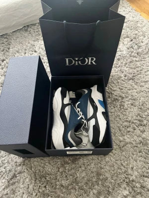 Dior B22 sneakers blå och svart vit  - Säljer ett par Dior B22 sneakers i blått, svart, vitt och grått. Skorna har chunky sula, meshpaneler och detaljer i läder samt textil. Klassisk Dior-logga på sidan och cool design som sticker ut. Perfekta för dig som gillar exklusiva sneakers.