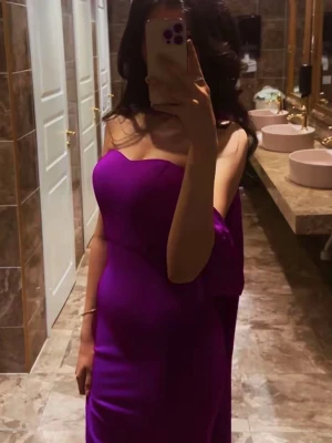 Lång lila klänning med scarfdetalj - Säljer en elegant långklänning i lila med figurnära passform. Klänningen har offshoulder-design och en matchande scarfdetalj runt halsen som ger en unik look. Perfekt för dig som vill sticka ut med en färgstark och stilren outfit nu till vår/sommar.