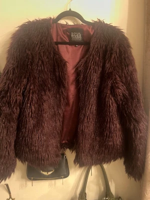 Mörklila fuskpälsjacka Soul River - Säljer en fluffig mörklila/vinröd fuskpälsjacka från Soul River. Jackan har en cool oversized look. Perfekt för dig som vill sticka ut med en trendig och tuff pälsjacka i vår.