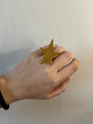 Guldfärgad ring med stjärnform - Cool statementring i metall med en stor stjärna i guldfärg. Perfekt accessoar för dig som vill sticka ut och ge din outfit en unik touch. Ringen har en modern och lekfull design som drar blickarna till sig. aldrig använt, den är sjusterbar 