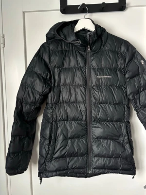 Svart dunjacka Peak Performance - Snygg svart dunjacka från Peak Performance med luva. Är i bra skick har endast några mindre fläckar vid kragen. Hör av dig vid frågor