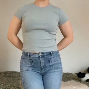 Ljusblå ribbad t-shirt - Säljer en ljusblå ribbad t-shirt med korta ärmar och rund hals. T-shirten har en tight passform och är tillverkad i ett mjukt, stretchigt material som sitter snyggt på kroppen. Perfekt att matcha med jeans eller kjol för en clean look. Säljer även en likadan i grön och en i beige