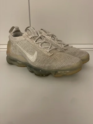 Nike Air Vapormax Flyknit vita sneakers - Storlek 40 passar mig som har 42. Nike Air Vapormax Flyknit sneakers i ljusgrått och vitt med stickad ovandel och genomskinlig sula. Snyggt stickat material, klassisk Nike Swoosh på sidan och innovativ dämpning i sulan. Perfekta för dig som gillar sportig och modern stil. 