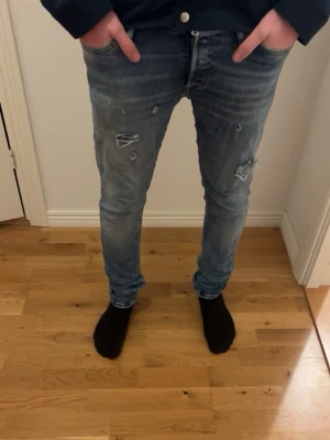 Blå slitna skinny jeans - Säljer ett par blå skinny jeans med slitningar och hål på låren och knäna. Jeansen har en tvättad look och fem klassiska fickor. Perfekta för en avslappnad och trendig stil. Skriv för mer info 