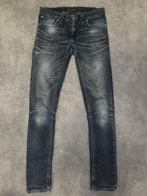 Mörkblå slim fit jeans från Nudie - Säljer ett par mörkblå slim fit jeans från Nudie Jeans med snygga slitningar och tvättade detaljer. Jeansen är i fint skick och har inga defekter. Hör av dig direkt vid frågor eller funderingar! :)